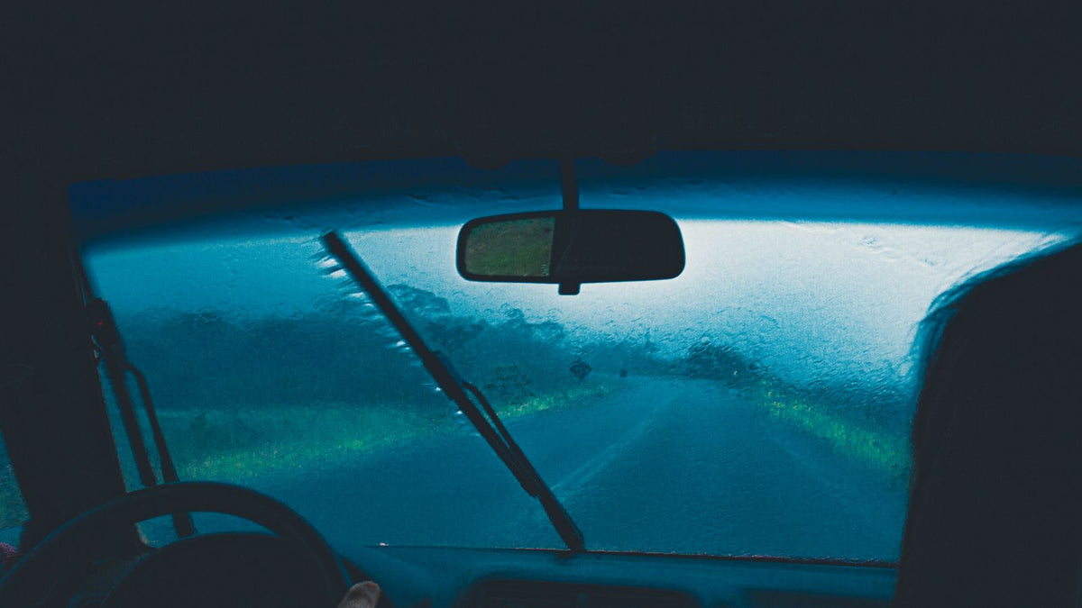 Car damp smell after monsoon India 2026 - view from inside a car through a rain soaked misted windscreen, water ingress and wet carpet padding diagnosis