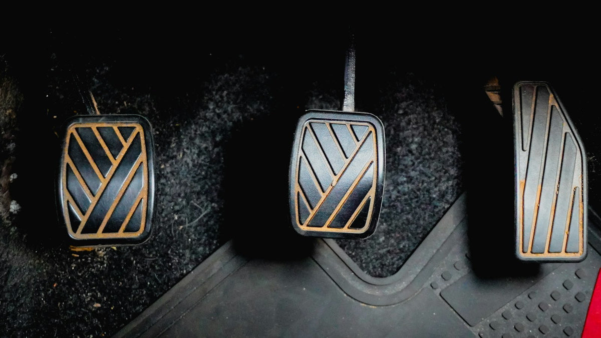 Clutch, brake and accelerator pedals in a car footwell with a rubber floor mat under the accelerator, showing how close a mat edge sits to the pedal
