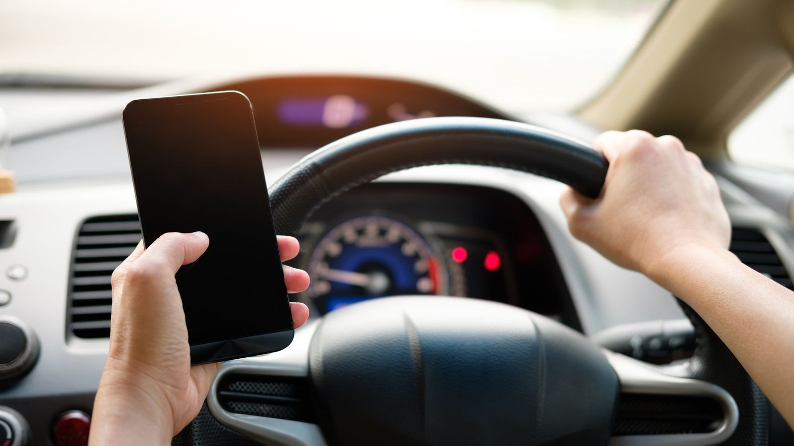 Person holding a smartphone next to a car steering wheel - car Bluetooth disconnecting fix guide India 2026, causes, the 10-minute fix, and the CarPlay upgrade